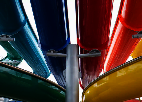 Blick von unten auf mehrere farblich unterschiedliche Rutschbahnen, getragen von Stahlstützen.