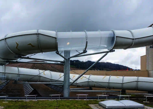 Teil einer weißen Wasserrutsche mit transparentem Acryl-Abschnitt auf einem Gebäudedach.