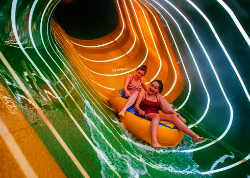 Zwei Frauen auf einem gelben Rutschreifen in einer ovalen Wasserrutsche.