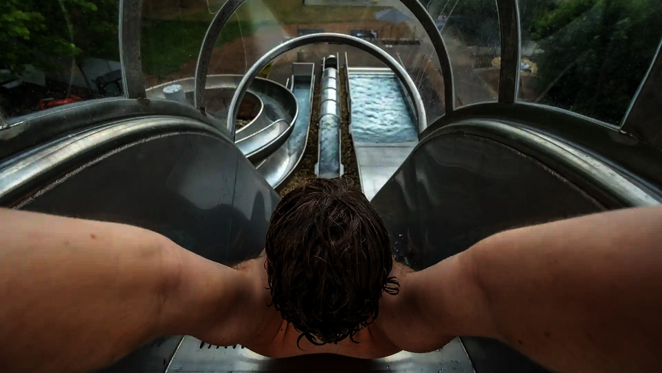 Junger Mann am Start einer Freifallrutsche mit Tunnel und Wasserbecken im Blick.