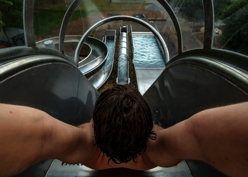 Junger Mann am Start einer Freifallrutsche mit Tunnel und Wasserbecken im Blick.