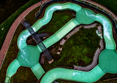 Luftaufnahme zeigt grünen Wildwasserfluss mit Brücken und Bepflanzung in der Mitte.