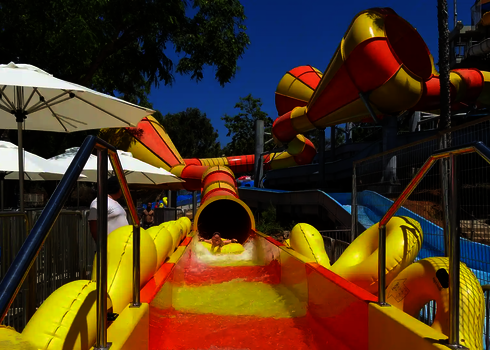 Kind rutscht aus dem Crazy Cone auf gelb-roter Bahn mit Wasser und Reifen.
