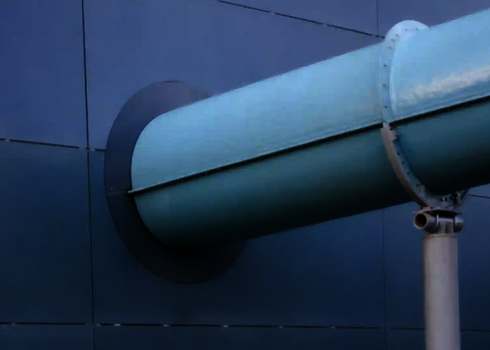 Blaue Wasserrutsche ragt durch eine glatte Fassade mit runder Durchführung.