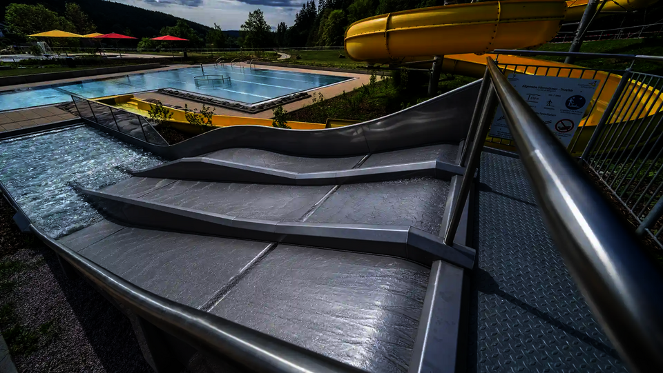 Dreibahnige Kinderrutsche Trio-Slide mit Wellen, daneben gelbe Spiralrutsche.