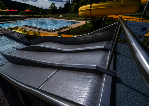 Dreibahnige Kinderrutsche Trio-Slide mit Wellen, daneben gelbe Spiralrutsche.