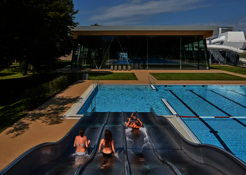 Drei Personen rutschen im Freibad nebeneinander eine Multilane Wasserrutsche hinunter.