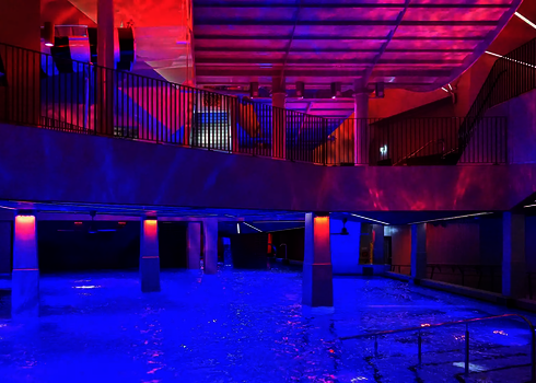 Innenbereich eines Schwimmbads mit Wasserbecken und farbenfroher Beleuchtung.