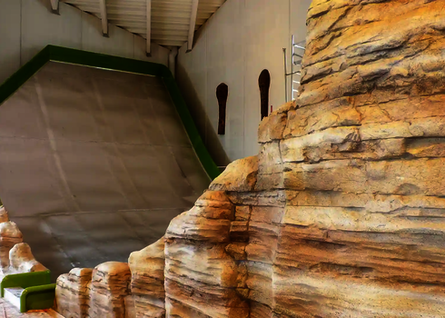 Blick auf die grüne Sidewinder Reifenrutsche zwischen künstlichen Felsen im Hallenbad.