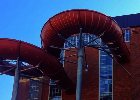 Die rote Wasserrutsche durchdringt die Gebäudefassade in Höhe großer Fenster.
