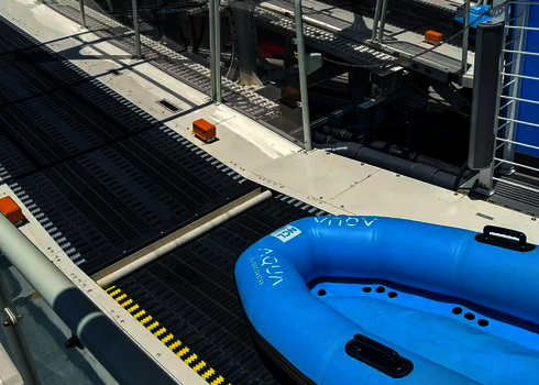 Blaues Doppel-Schlauchboot liegt auf einem schwarzen Gurtförderband an Deck.