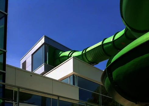 Grüne Wasserrutsche mit Fassadendurchdringung verläuft aus modernem Glasgebäude.