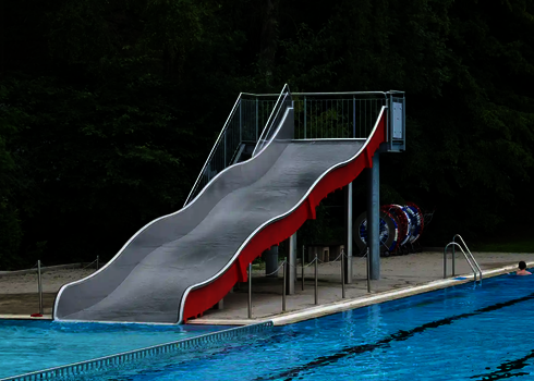 Eine Breitwellenrutsche mit roter Seitenwand, die in ein Schwimmbecken mündet.