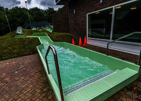 Austrittsbereich des Wildwasserflusses mit Einstiegstreppe vor einem modernen Gebäude.
