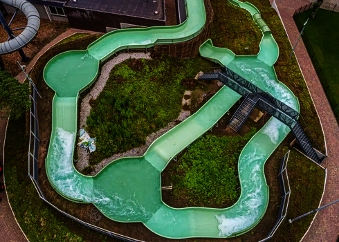 Obenansicht auf kurvigen Wildwasserfluss mit Grünfläche und Fußwegen ringsum.