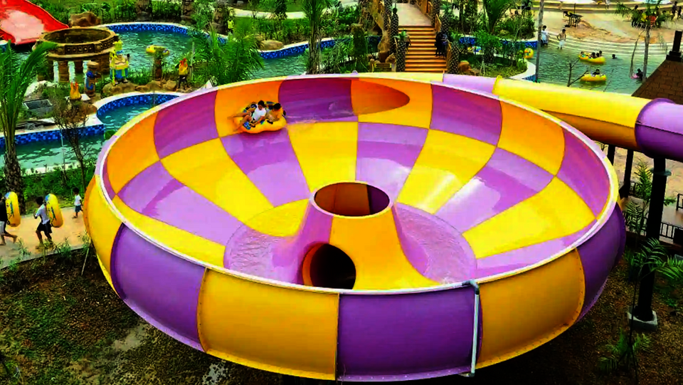 Raft Bowl in einem Wasserpark, umgeben von Besuchern, Palmen und weiteren Rutschen.