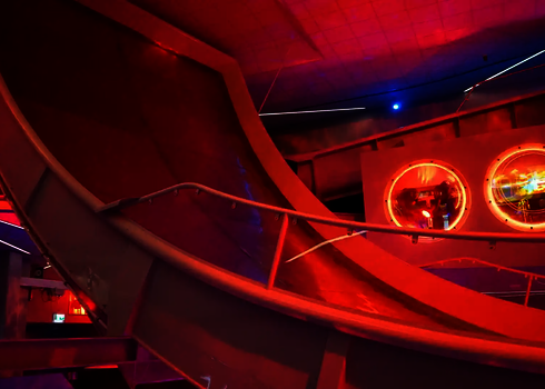 Nahaufnahme einer rot beleuchteten Boomerang-Rutsche mit kreisförmigen Lichtquellen.