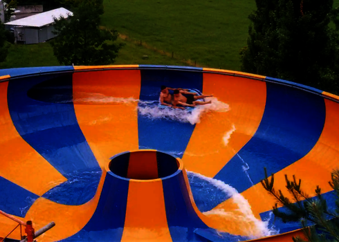 Zwei Personen rutschen auf einem Reifen in einer bunten Wasserrutsche über einer Wiese.