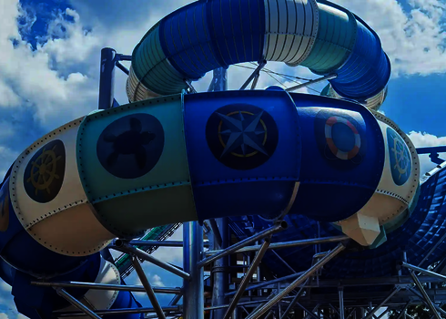 Blau-weiße Rutsche mit Tageslichtmotiven wie Schildkröte, Kompass und Rettungsring in Bogenform.