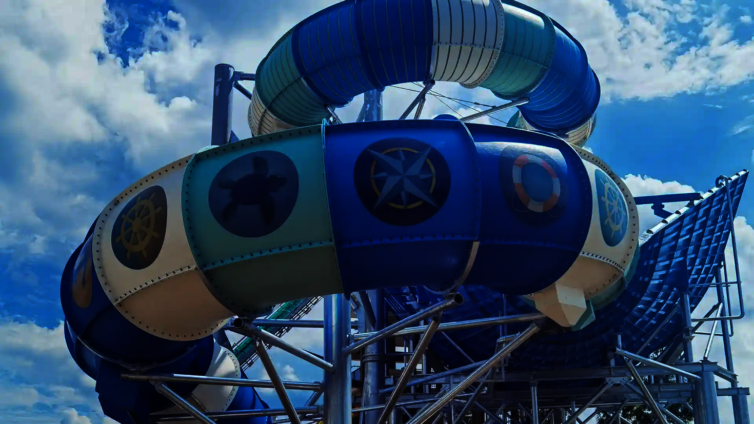 Blau-weiße Rutsche mit Tageslichtmotiven wie Schildkröte, Kompass und Rettungsring in Bogenform.