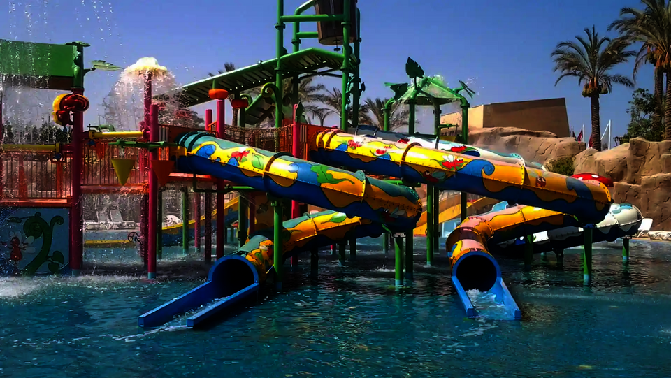 Wasserspielstruktur mit bunten Rutschen, die in einem blaues Schwimmbecken führen.