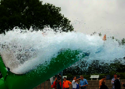 Ein großer Wasserschwall kommt aus einem grünen Cannonball, im Hintergrund schauen mehrere Personen zu.