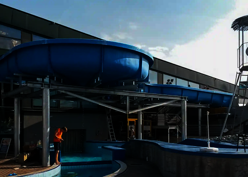 Blauer Wildwasserfluss führt entlang einer Glasfassade in den Außenbereich eines Bads.