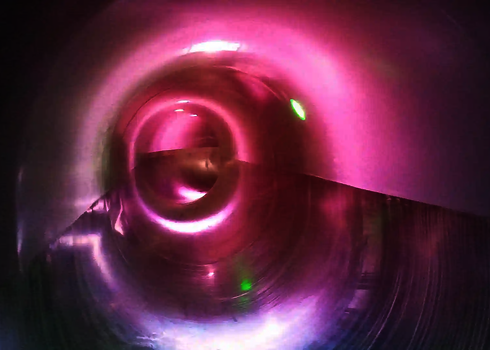 Blick in eine Wasserröhre mit rosa Lichtreflexionen und grünem LED-Punkt.