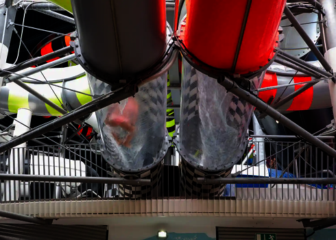 Zwei transparente Röhrenrutschen mit Wasserlauf starten nebeneinander von einer Plattform.