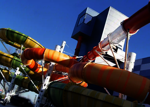 Außenaufnahme eines grünen Family Twisters und weiterer Wasserrutschen vor blauen Gebäuden.