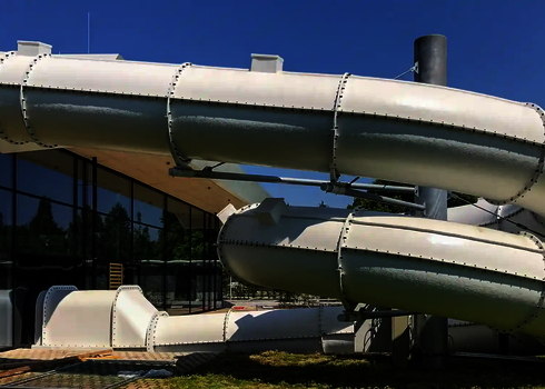 Blick auf eine weiße Wasserrutsche des Typs RR1400 vor einem Glasgebäude.