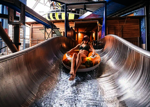 Frau rutscht auf einem gelben Reifen auf einer Wasserrutsche und trägt eine VR-Brille.
