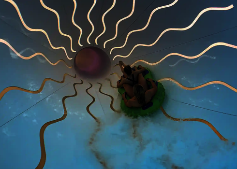 Zwei Personen auf einem grünen Reifen rutschen durch einen Crazy Cone mit Leuchteffekten.