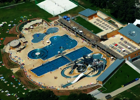 Vogelperspektive auf einen Outdoor-Wasserpark mit Schwimmbecken, Wasserrutschen und Liegeflächen.