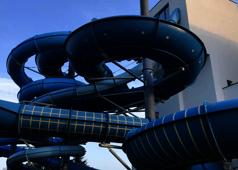 Mehrere blaue Röhren der Family Twister Rutsche schlängeln sich um einen weißen Gebäudekomplex.