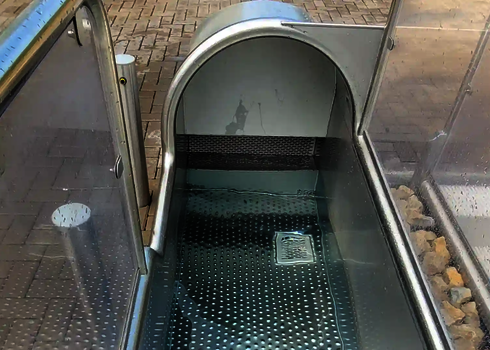 Slide exit with water, stainless steel floor and grating, surrounded by clear side walls.