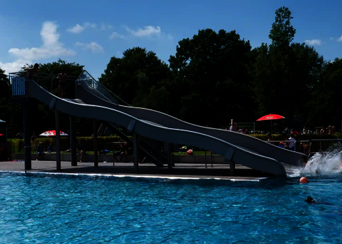Breitwellenrutsche in einem Freibad, hinter einen blauen Schwimmbecken.