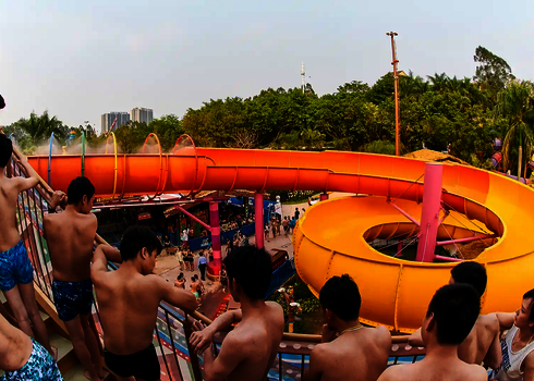 Mehrere Personen stehen an einem Geländer und schauen auf eine gelbe Wasserrutsche des Typs RR2700.