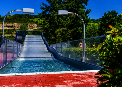 Blick auf eine Breitwellenrutsche mit Auslaufbecken, im Hintergrund grüne Felsen.