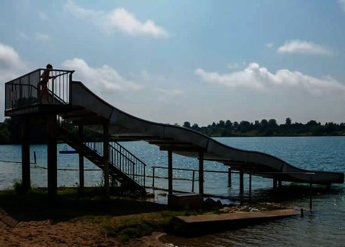 Eine Breitwellenrutsche an einem Badesee, ein Kind steht oben am Startbereich.