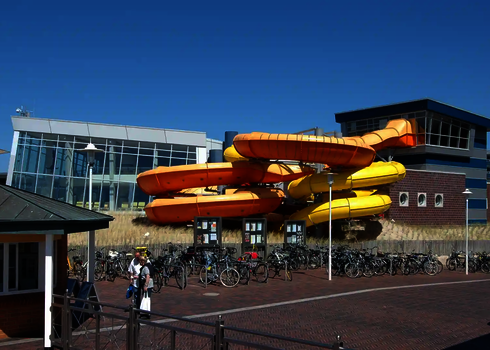 Gelbe und orange Family Twister Röhren an einem Schwimmbad mit Fahrradständern.