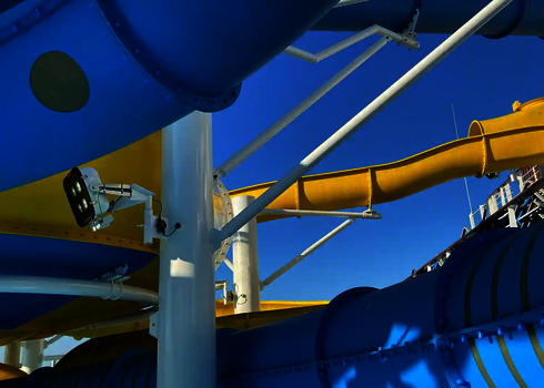 Weiße Stahlträger stützen eine gelbe und blaue Wasserrutsche unter blauem Himmel.