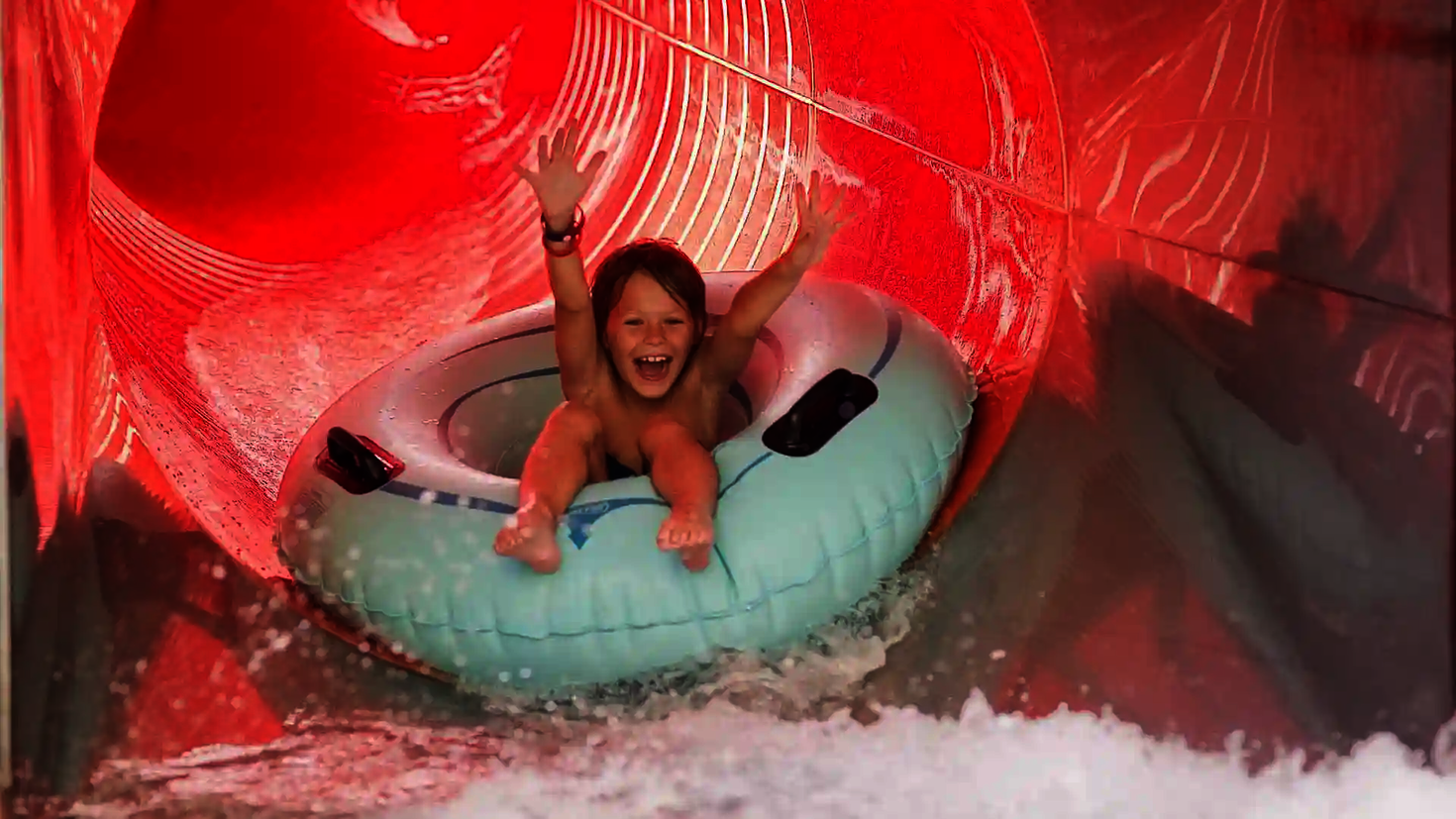 Junge rutscht lachend und mit erhobenen Händen in einen hellblauen Schwimmreifen.