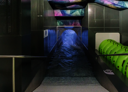 Wave-shaped illuminated slide exit with green tyres on metal mesh.