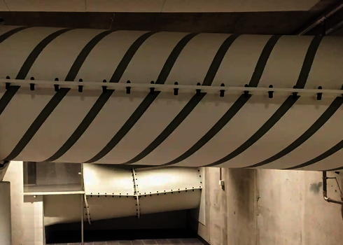 Weiß-graue Spiralsegmente einer Wasserrutsche verlaufen durch Kellerraum.