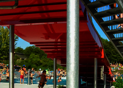 Sicht unter einer roten Breitwellenrutsche, die sich in einem Schwimmbad mit vielen Badegästen befindet.