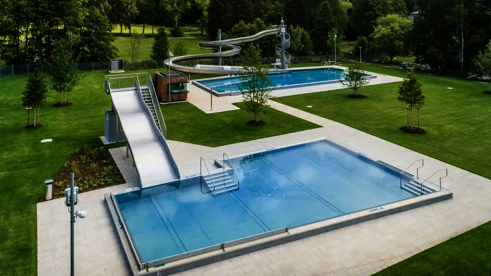 Blick auf ein sauberes Freibad mit einer Breitwellenrutsche, gelegen im Grünen.