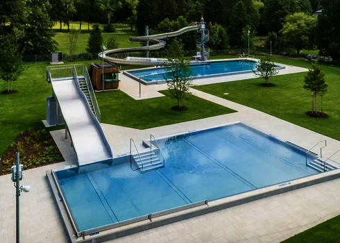 Blick auf ein sauberes Freibad mit einer Breitwellenrutsche, gelegen im Grünen.