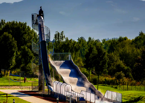 Freifall mit transparenter Überdachung und Breitwellenrutsche in grüner Parkumgebung.