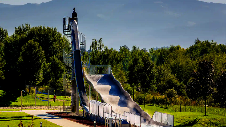 Freifall mit transparenter Überdachung und Breitwellenrutsche in grüner Parkumgebung.